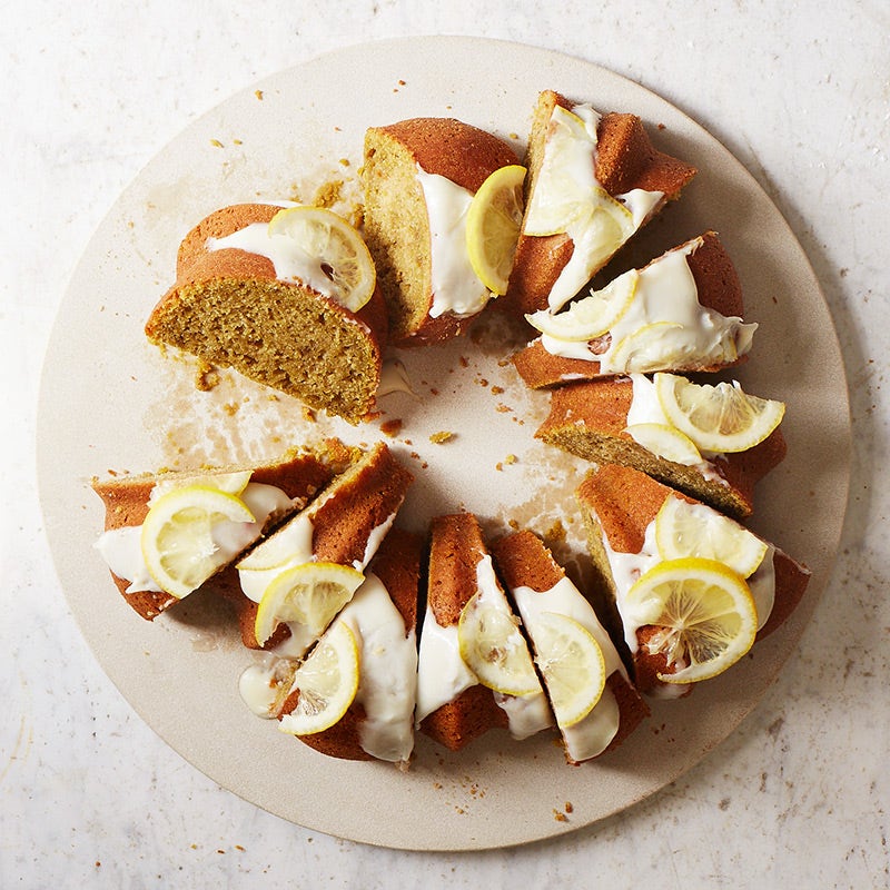 lemon bundt cake on a circular platter drizzled with glaze and topped with lemon slices