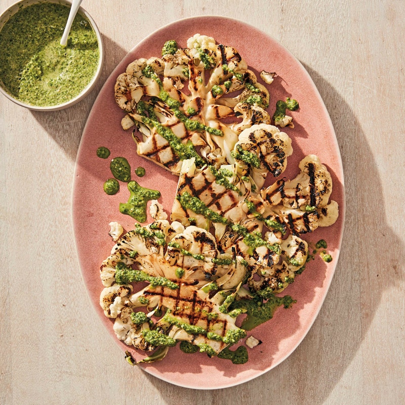 large, oval pink platter topped with grilled cauliflower steaks, drizzled with a homemade pesto sauce