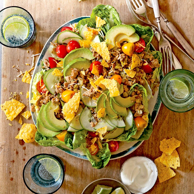 large square serving platter topped with lettuce, tomato, cucumber, avocado, sauteed ground turkey, tortilla chips, and cheese, served with sour cream and lime wedges