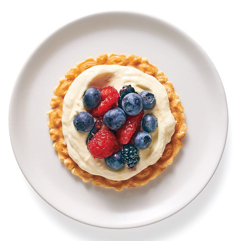 small white plate with a lemon pizzelle cookie topped with creamy lemon curd and fresh mixed berries