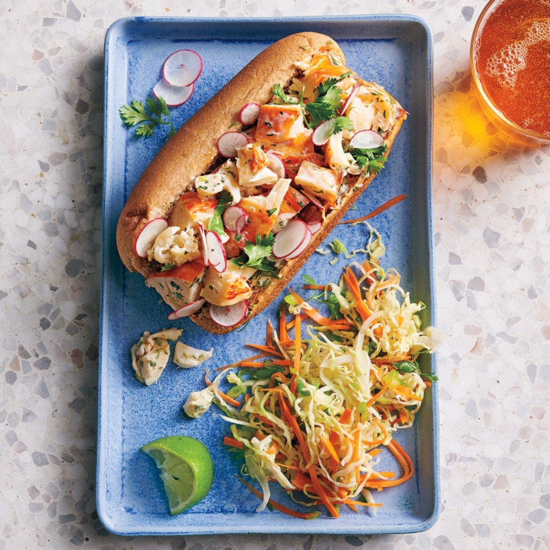 Small rectangular blue plate topped with a lobster roll sandwich, some optional slaw, and a lime wedge