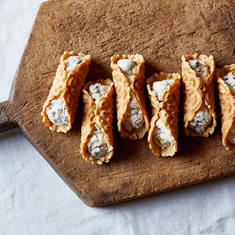 wooden serving board topped with cannolis made with vanilla pizzelle cookies and a vanilla-ricotta mixture with chopped chocolate