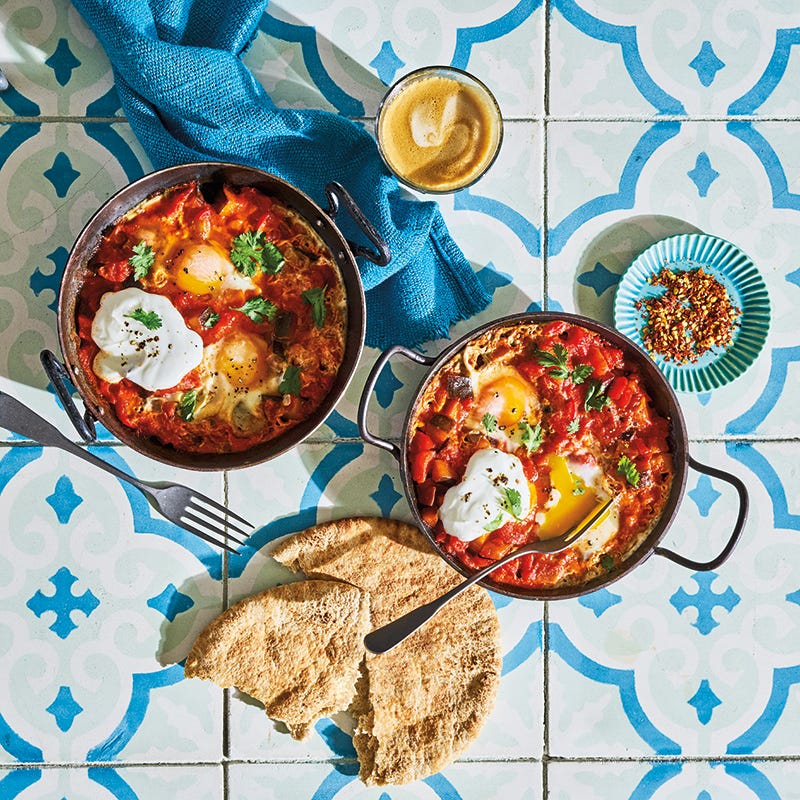 spicy tomato sauce and poached eggs cooked and served in a skillet, with pita bread on the side