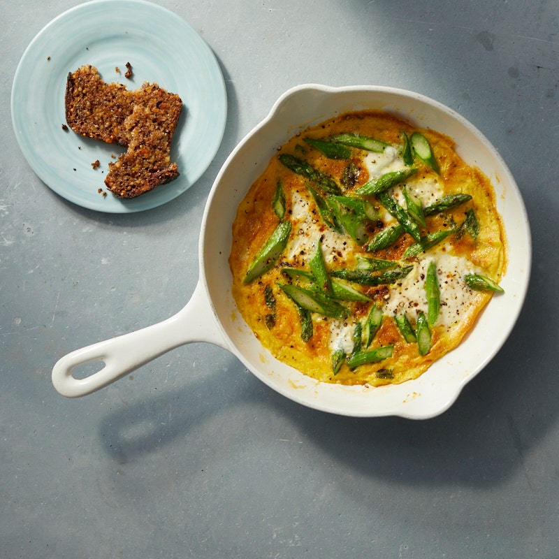 asparagus and goat cheese frittata in a small white ovenproof skillet and a small plate with sliced bread on the side
