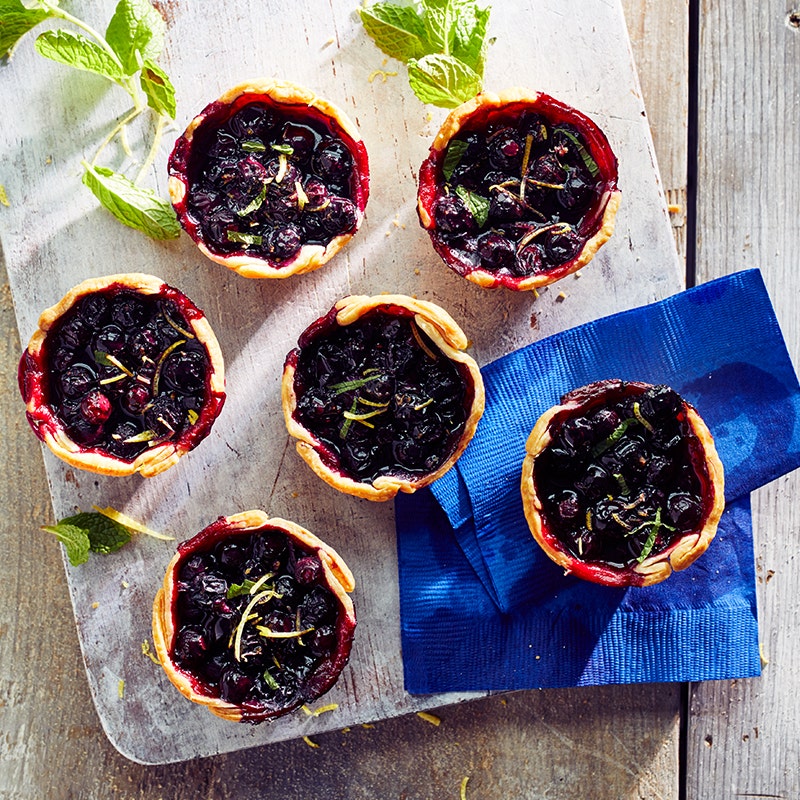 Six individual blueberry pies on a wooden board