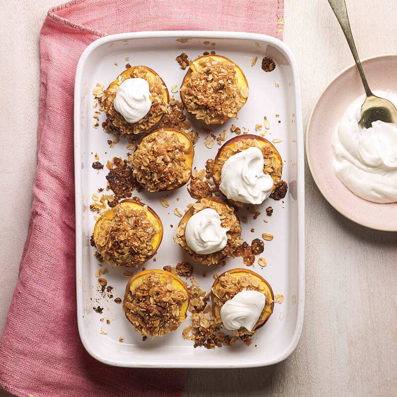 Baked peach halves sprinkled with an almond-oat topping and optional yogurt served on a white rectangular platter