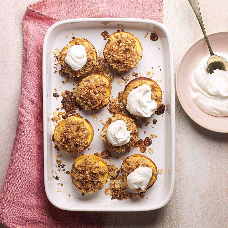 Baked peach halves sprinkled with an almond-oat topping and optional yogurt served on a white rectangular platter