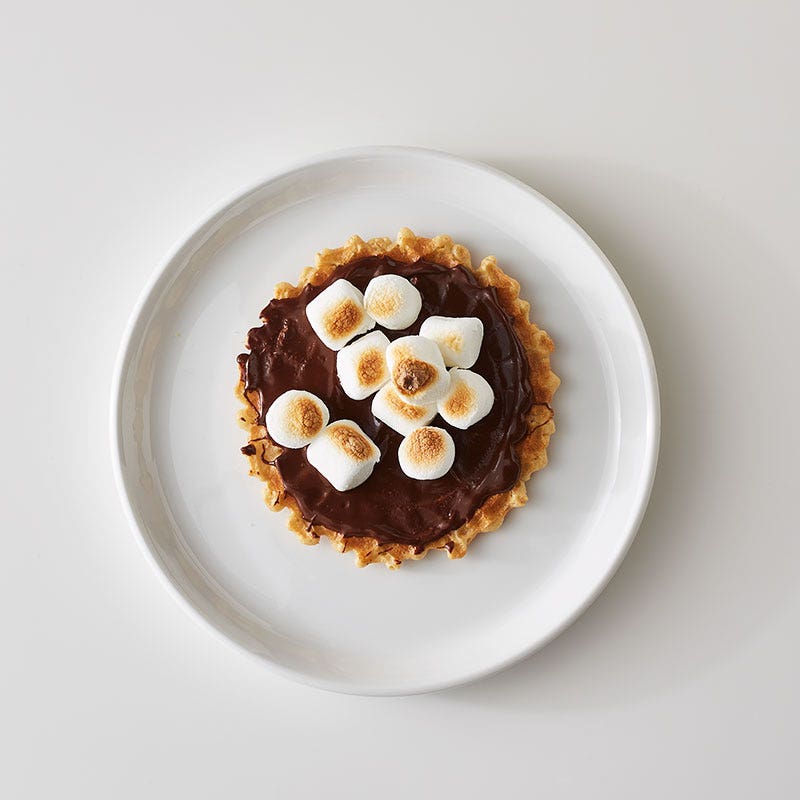 Small white plate with a vanilla pizzelle cookie topped with melted chocolate and toasted mini marshmallows