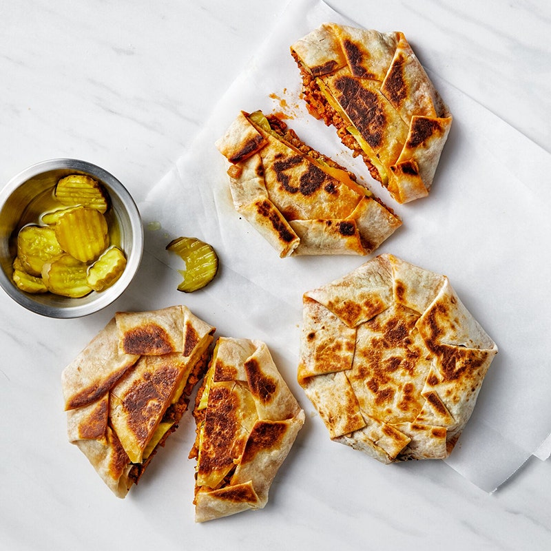image of 3 sloppy Joe crunch wraps on parchment paper with a small bowl of pickles on the side