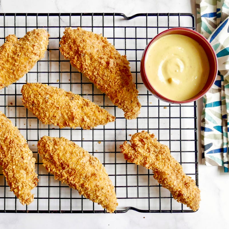 Tortilla chip–crusted chicken tenders on a cooling rack with a small bowl of honey mustard on the side