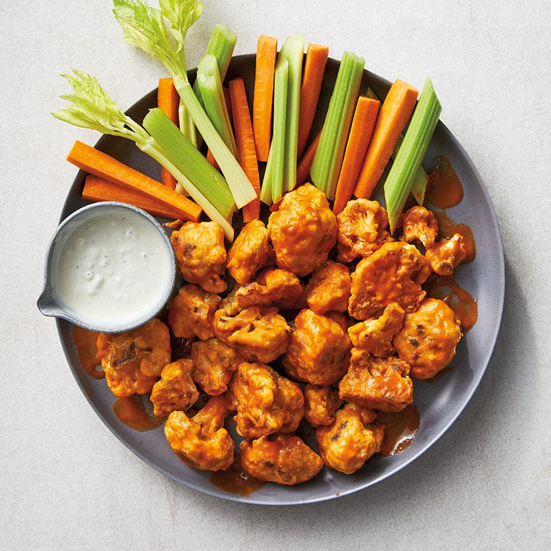 Large round serving plate topped with roasted Buffalo cauliflower bites, raw carrot and celery sticks, and a small bowl of blue cheese dipping sauce