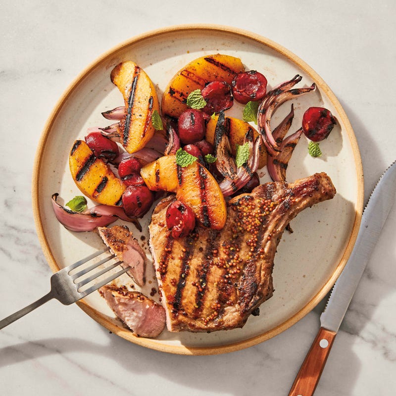 Round dinner plate topped with a grilled mustard-glazed pork chop, sliced onion, peach wedges, and cherries