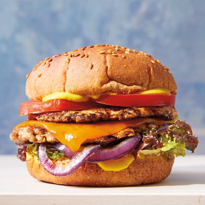 double smashed turkey burger on a bun with sliced cheese, sliced tomato, lettuce, cooked red onion, and mustard