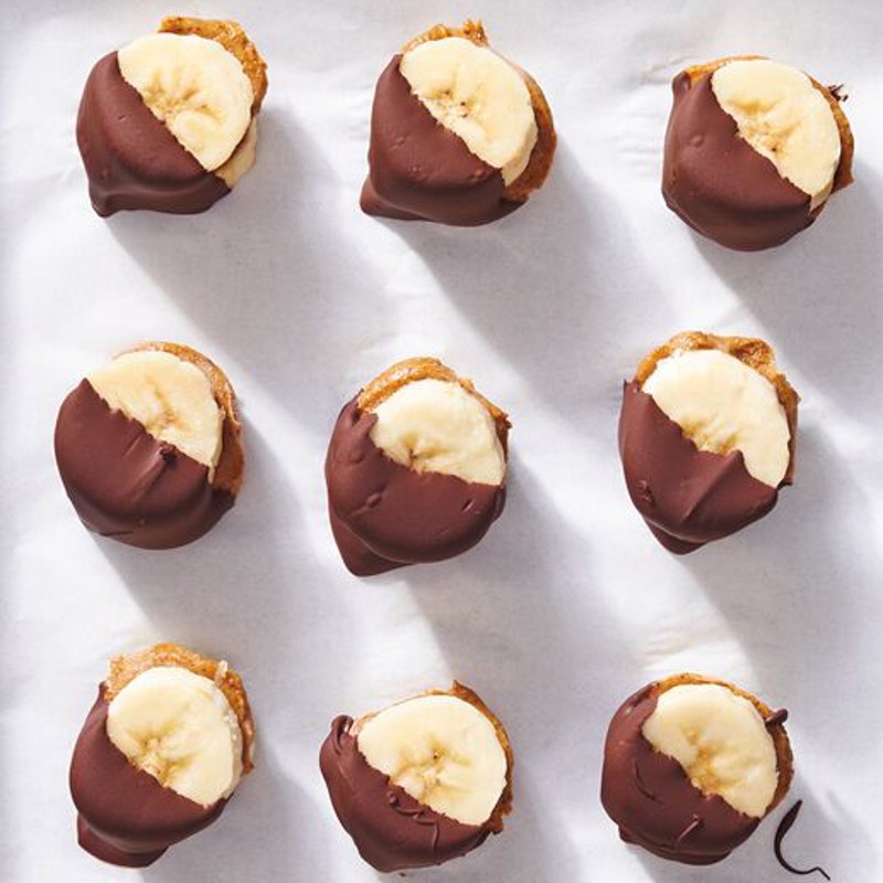 peanut butter sandwiched between banana slices that are half-dipped in melted chocolate and then frozen on parchment paper