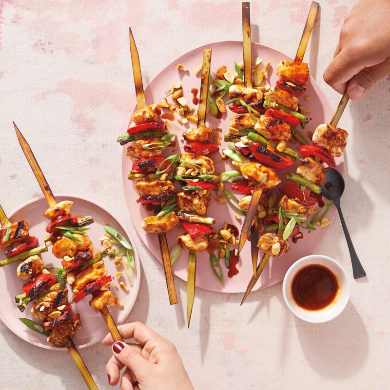 pink oval platter topped with grilled Asian chicken and vegetable skewers and a small bowl of dipping sauce