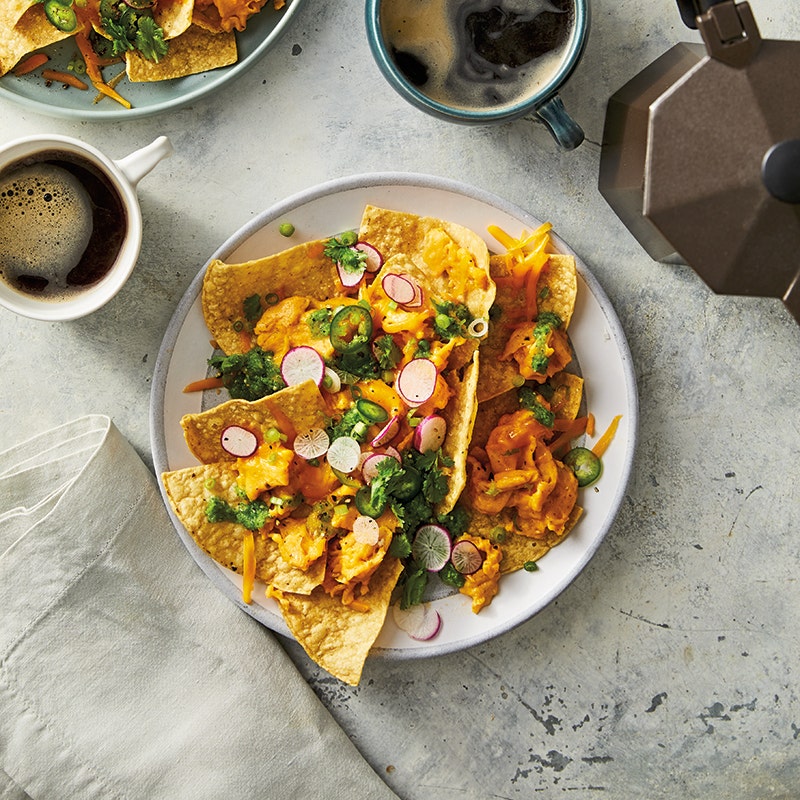 Round white plate topped with tortilla chips, scrambled eggs, cheese, salsa, and scallions