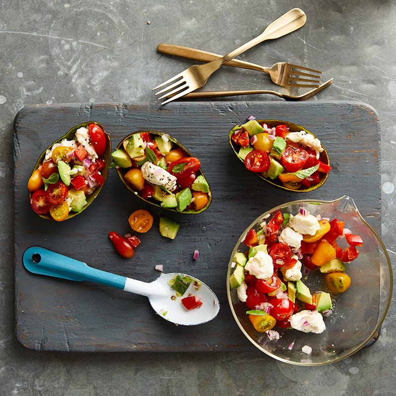 Small wooden board topped with avocado, tomato, pepper, and cheese-stuffed avocado halves