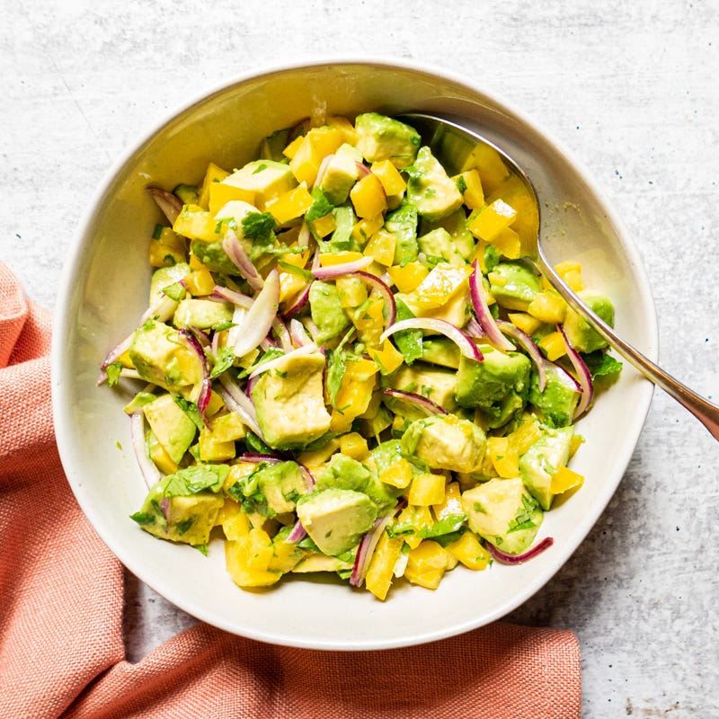 Round serving bowl with avocado, red onion, and yellow pepper tossed with lime juice, salt, and pepper