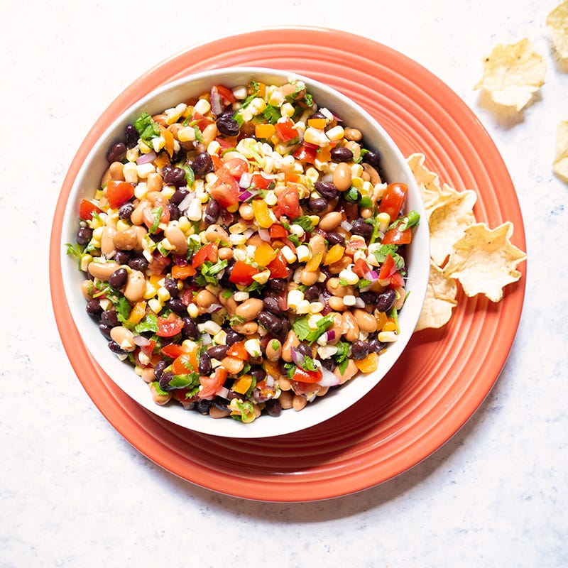 a large white serving bowl filled with pinto beans, black beans, corn, tomatoes, peppers, and onion, tossed with a lime vinaigrette