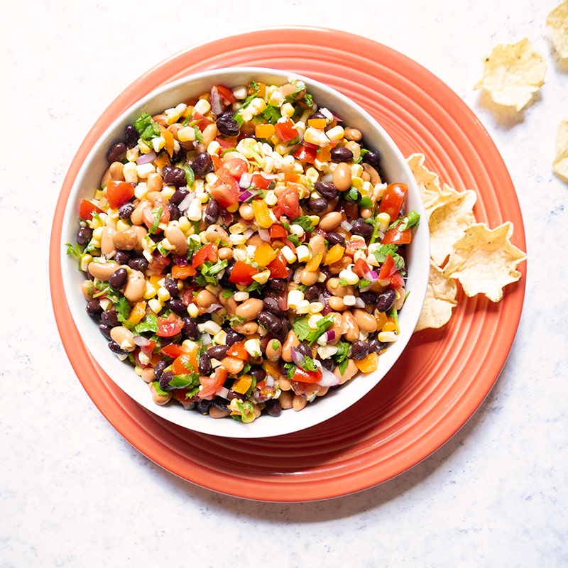 a large white serving bowl filled with pinto beans, black beans, corn, tomatoes, peppers, and onion, tossed with a lime vinaigrette