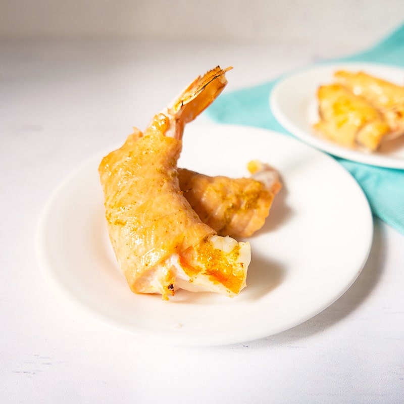 a small white plate topped with two salmon-wrapped shrimp cooked with a lime-honey glaze