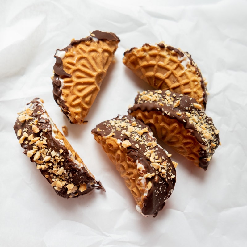 vanilla pizzelle cookies folded like a taco shell, filled with vanilla ice cream and coated with melted chocolate that hardens and is sprinkled with chopped peanuts